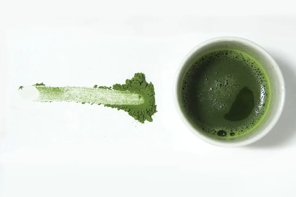 A smear of matcha powder beside a cup of whisked matcha