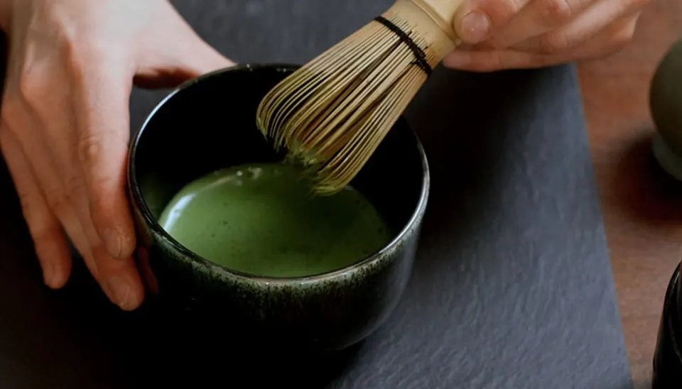 Hands whisking matcha in a black bowl